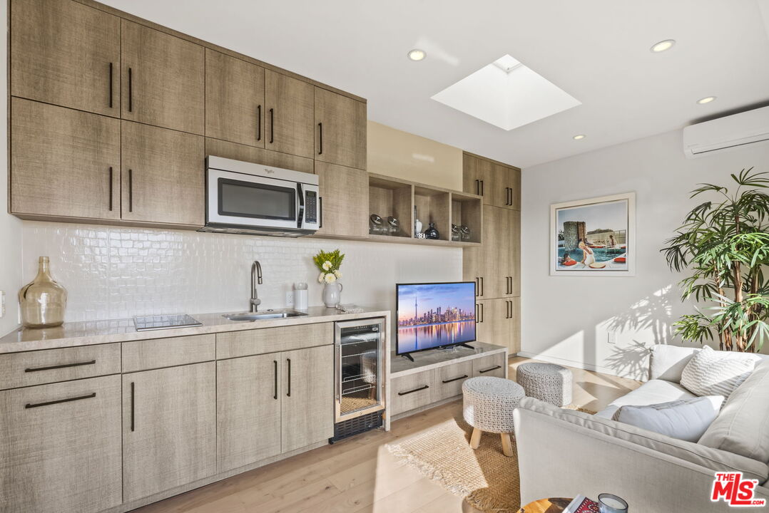 Kitchen and living area with wood cabinetry, a skylight, beverage refrigerator, and white sofa.