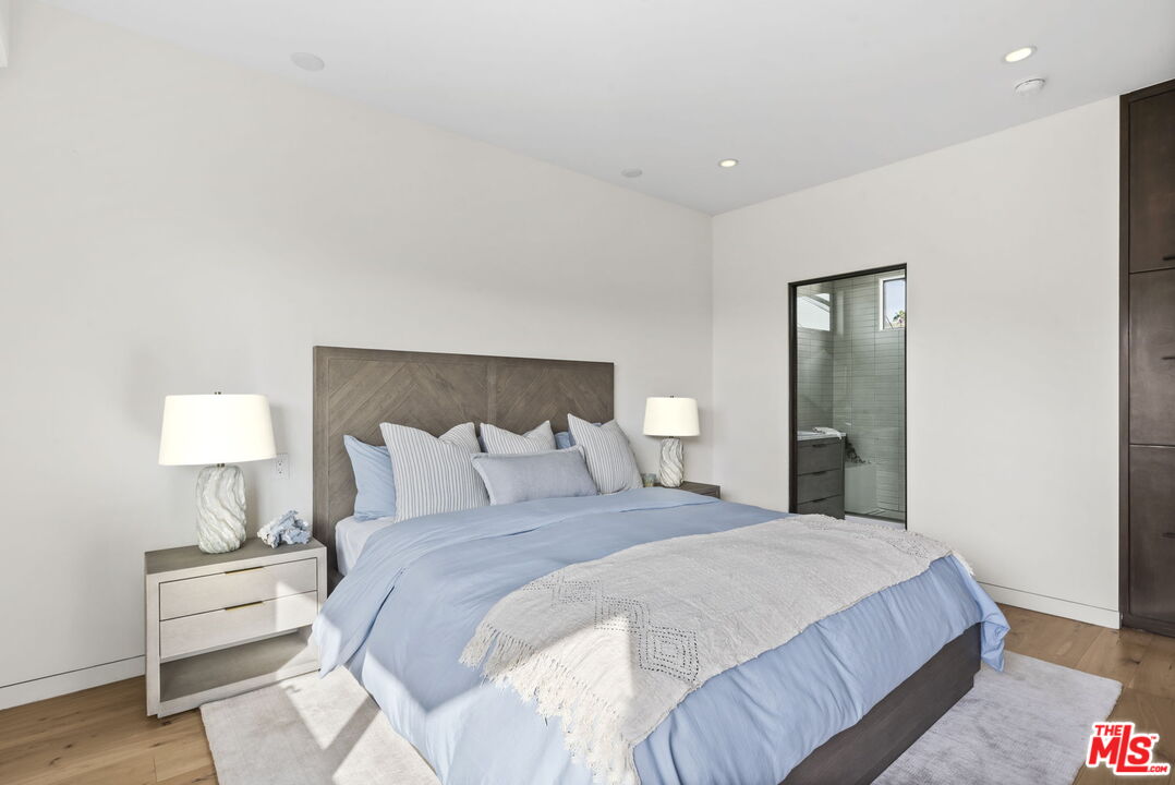 Bedroom with pale blue bedding, a textured white throw, and a glass doorway to the bathroom.