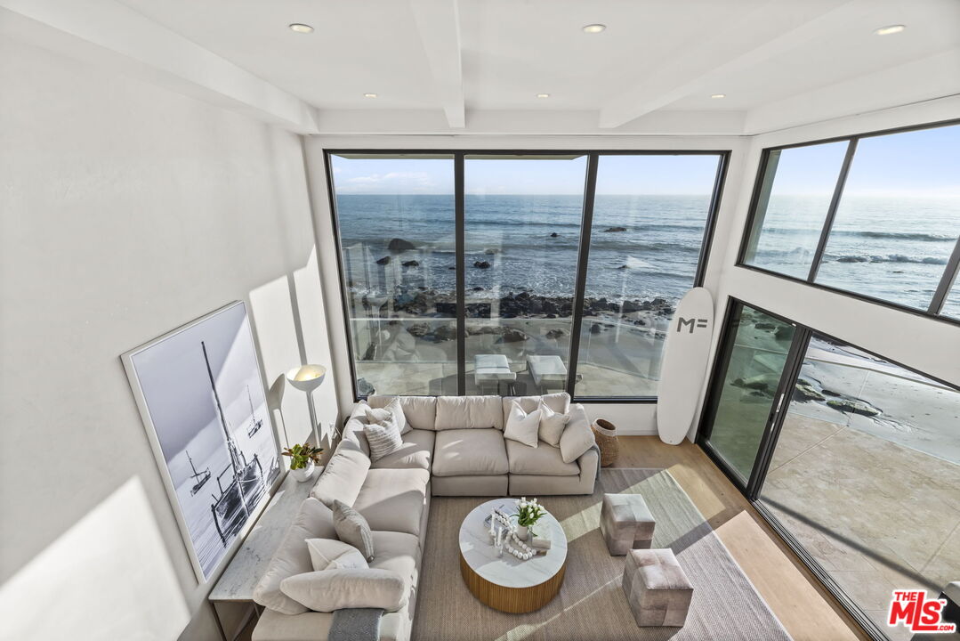 Oceanfront living room with a sectional sofa, floor-to-ceiling windows, and views of the rocky shoreline.