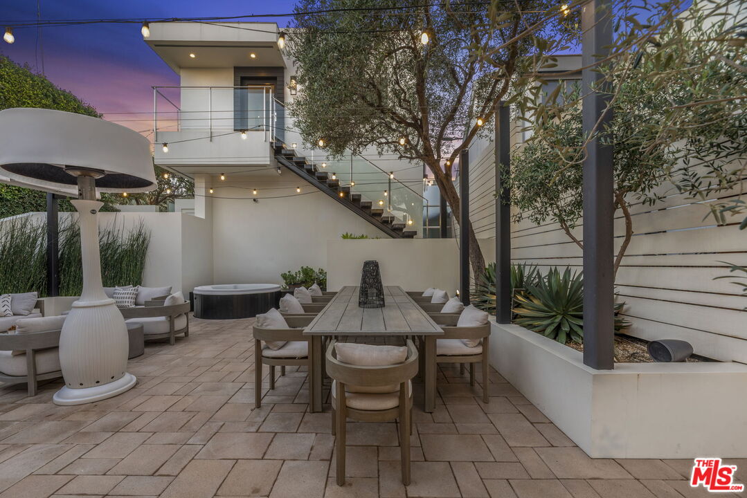 Modern home patio with outdoor dining, lounge seating, a hot tub, and string lights at dusk.