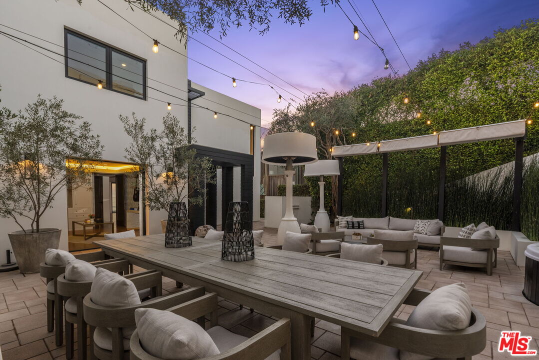 Modern home patio with a large dining table, lounge seating, string lights, and a canopy pergola.
