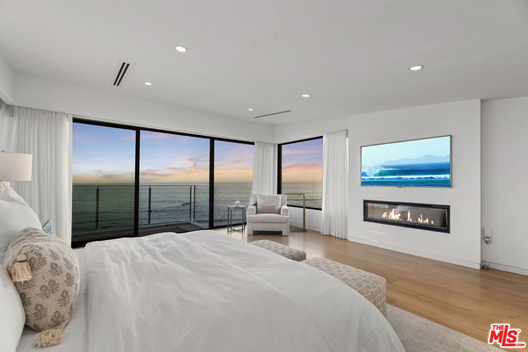Ocean-view bedroom with a large bed, glass balcony doors, and a linear fireplace.