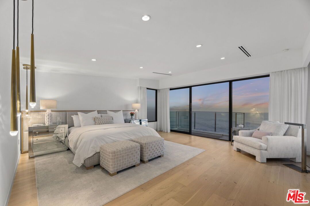 Ocean-view bedroom with a king bed, upholstered benches, and sliding glass doors at dusk.