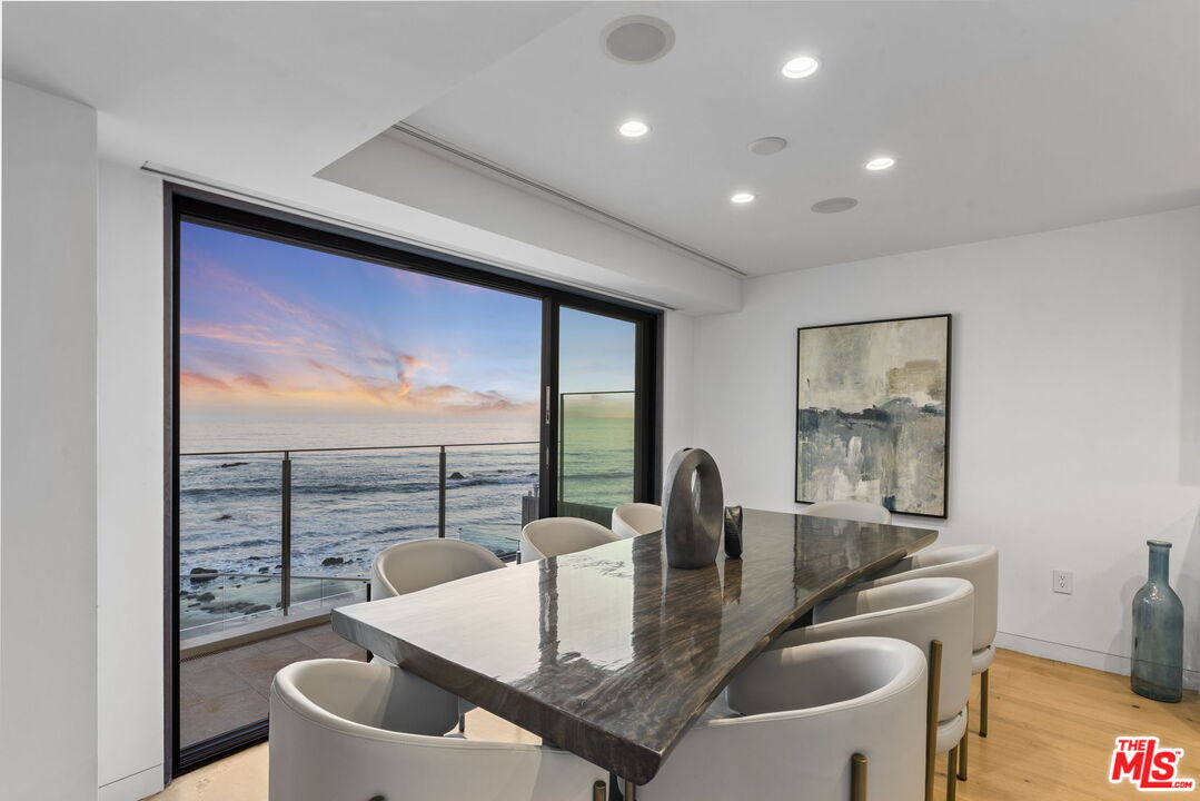 Dining room with a stone table and ocean views through sliding glass doors.