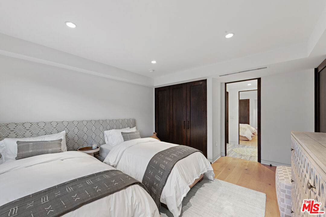 Bedroom with two white beds, a patterned headboard, dark built-in closet, and light wood floors.