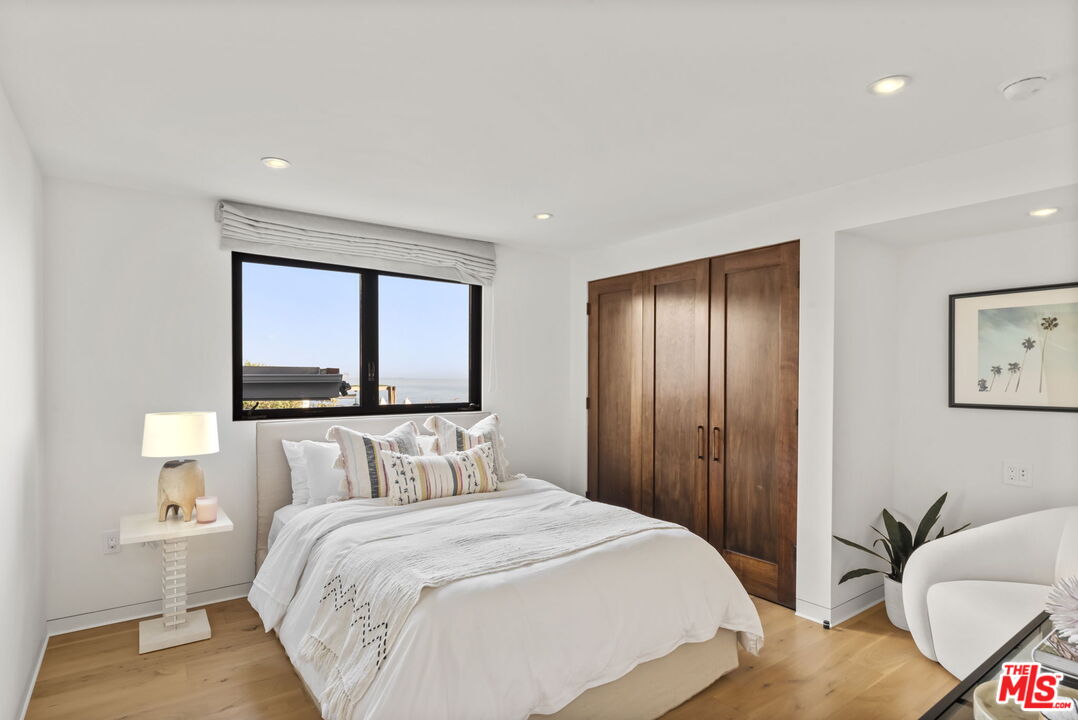 Staged bedroom with a white bed and ocean view through the window.