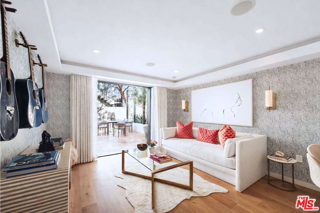 Living room with a white sofa, coral cushions, displayed guitars, and sliding doors to a patio.