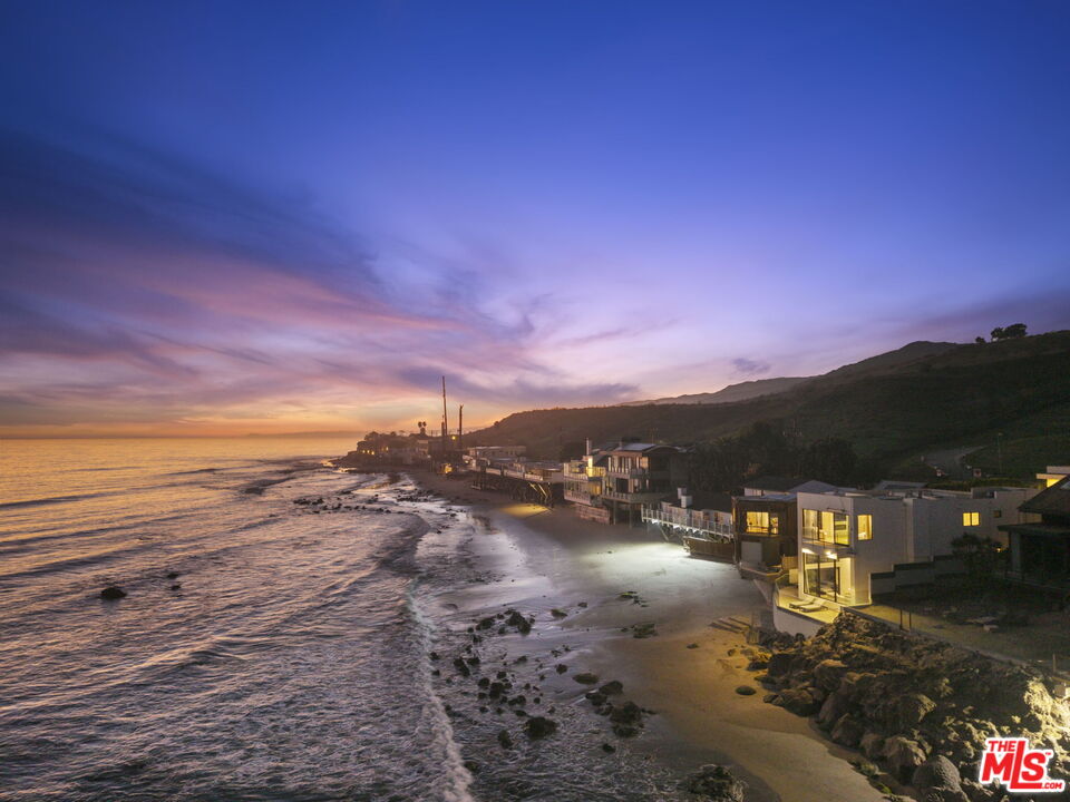 Beachfront homes line a rocky Malibu shore beneath a colorful dusk sky.