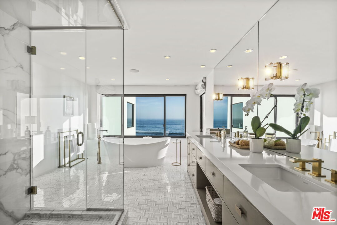 Modern bathroom with a freestanding tub and ocean view, glass shower, and double vanity.