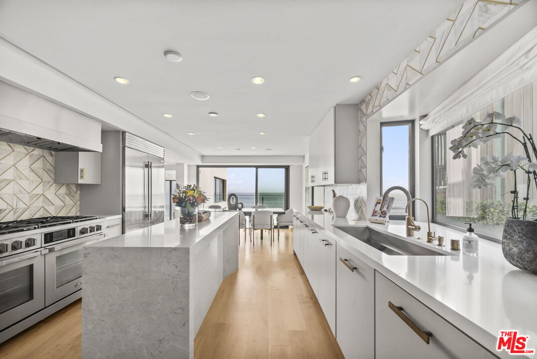 Bright modern kitchen with a long stone island, stainless appliances, and ocean view.