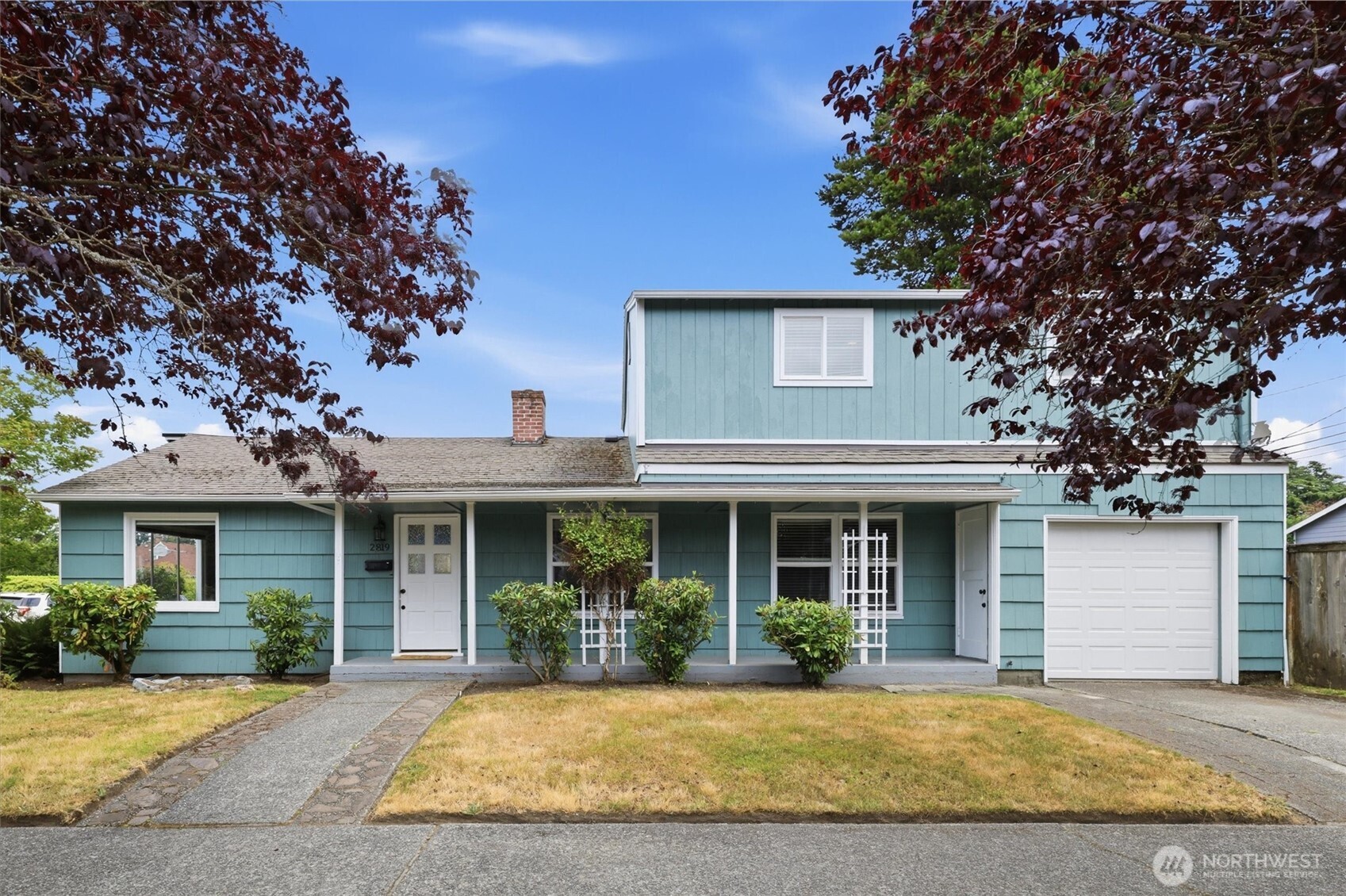 Blue two-story house with a covered porch and attached garage, framed by burgundy-leaf trees.