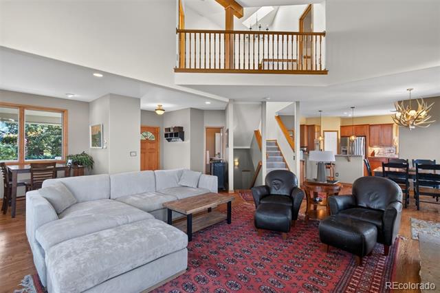 Living room with a gray sectional, black leather chairs, red patterned rug, and vaulted ceiling with loft railing.