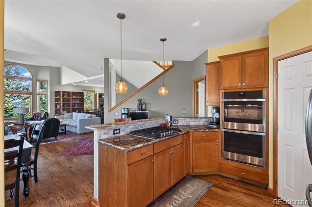 Open-plan kitchen with a granite island, gas cooktop, wood cabinetry, and stainless-steel double ovens.