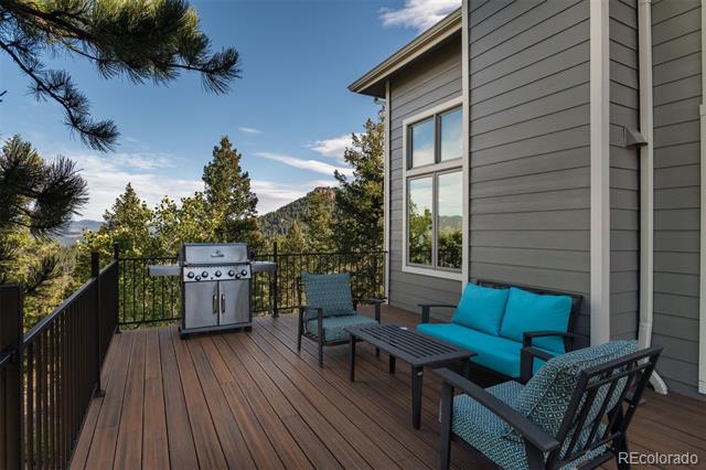 Furnished wooden deck with turquoise seating, a stainless steel grill, and mountain views.