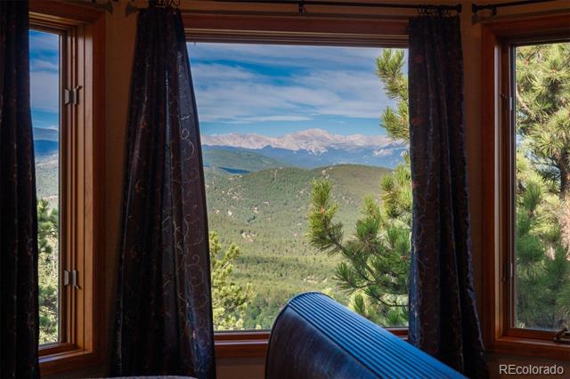 Interior window view of forested mountain foothills, framed by dark curtains and a blue chair.