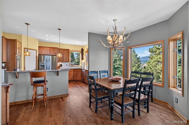 Open dining area with antler chandelier, adjoining kitchen, and mountain views through large windows.