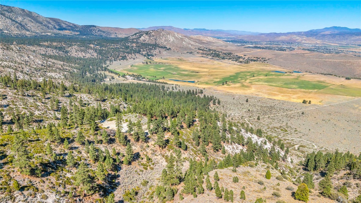Aerial view of wooded mountain land overlooking a broad valley and distant ranges.