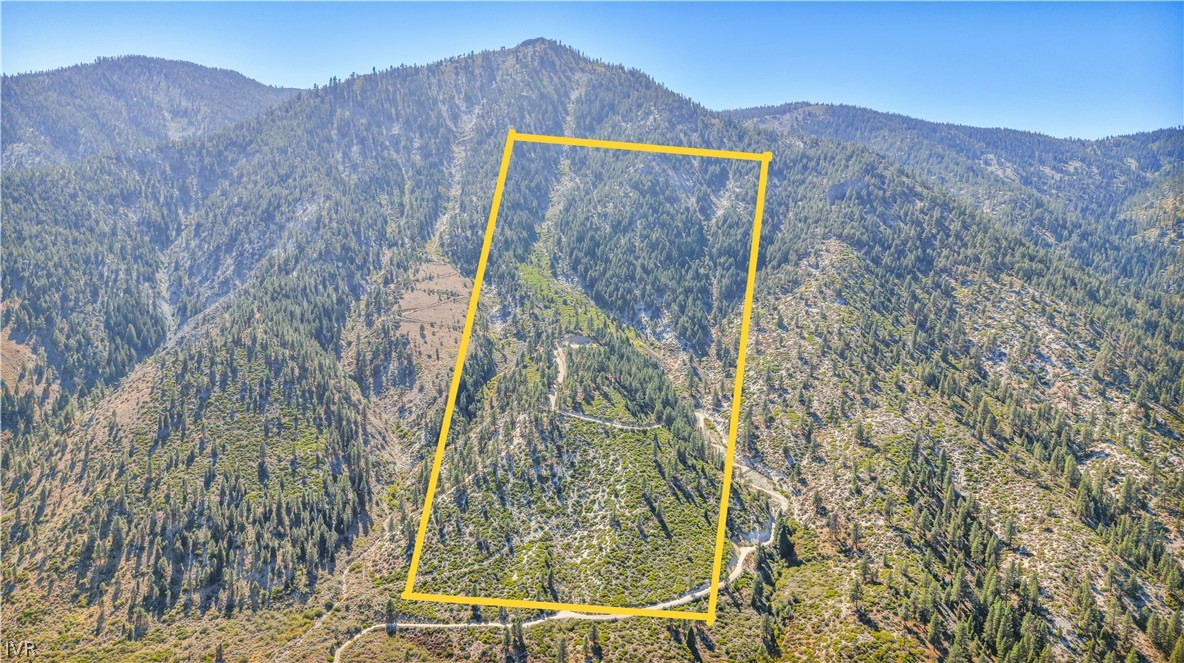 Undeveloped mountain parcel outlined in yellow, surrounded by wooded ridges and a winding access road.