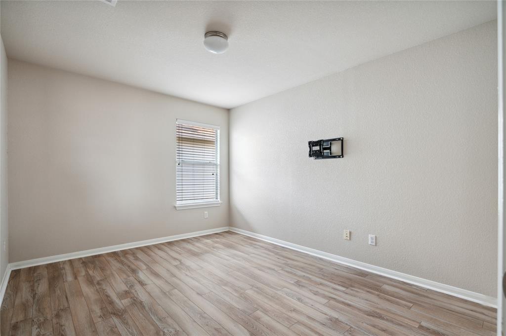 Empty room with wood-look flooring, window blinds, and a wall-mounted TV bracket.