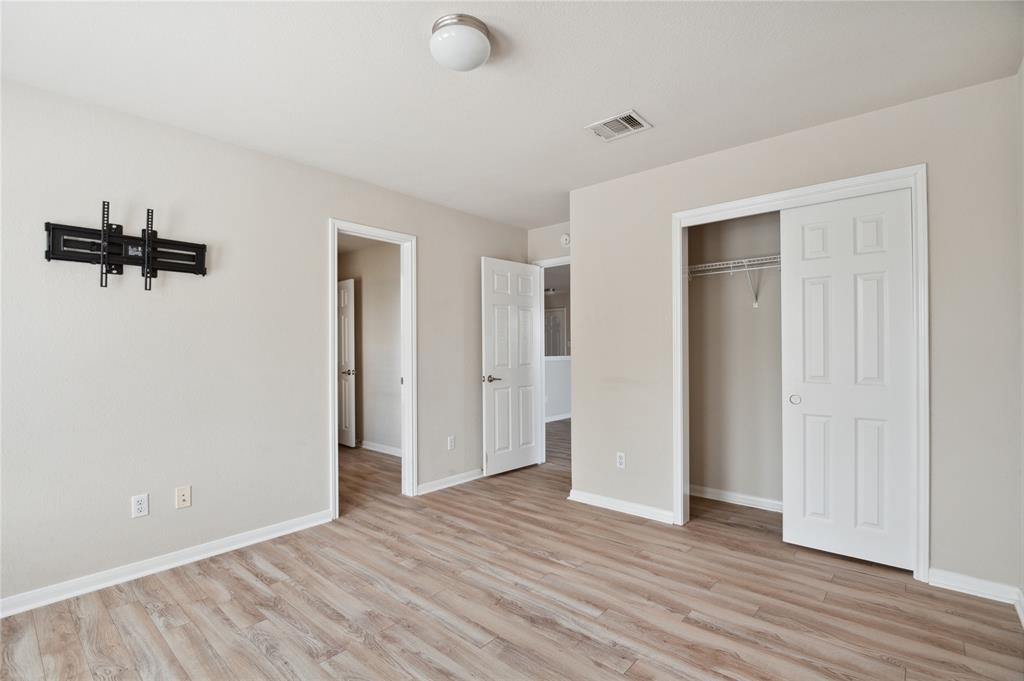 Empty bedroom with wood-look flooring, a wall-mounted TV bracket, and an open closet.