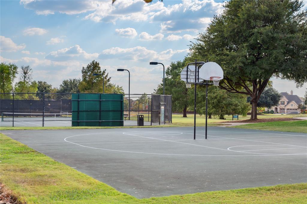 Outdoor basketball court beside fenced tennis courts, with mature trees in the background.