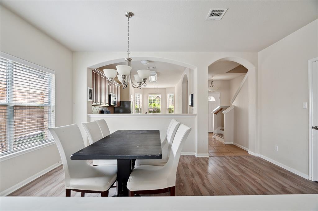 Dining area with a dark table and white chairs beside an arched opening to the kitchen.