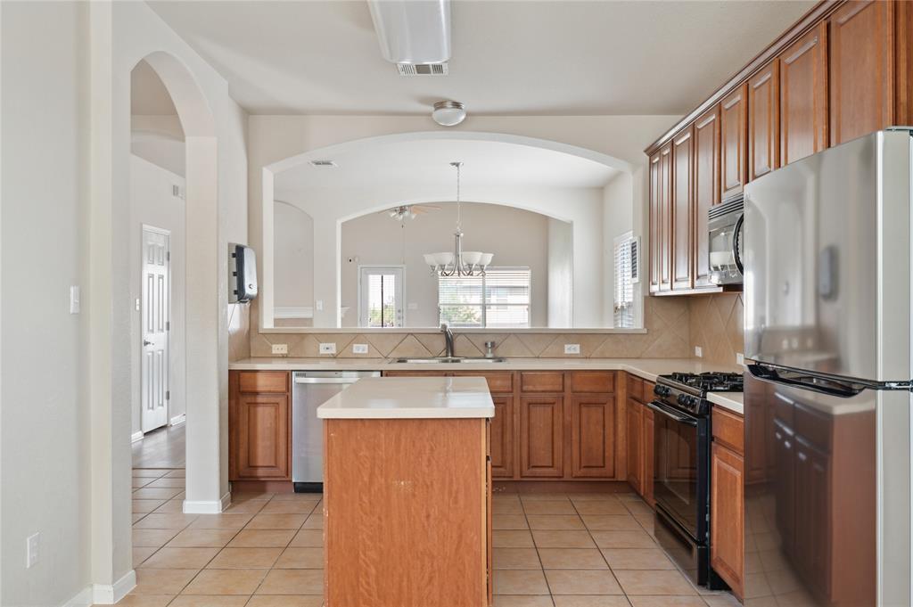 Kitchen with warm wood cabinets, stainless steel appliances, and a central island beneath an arched opening.