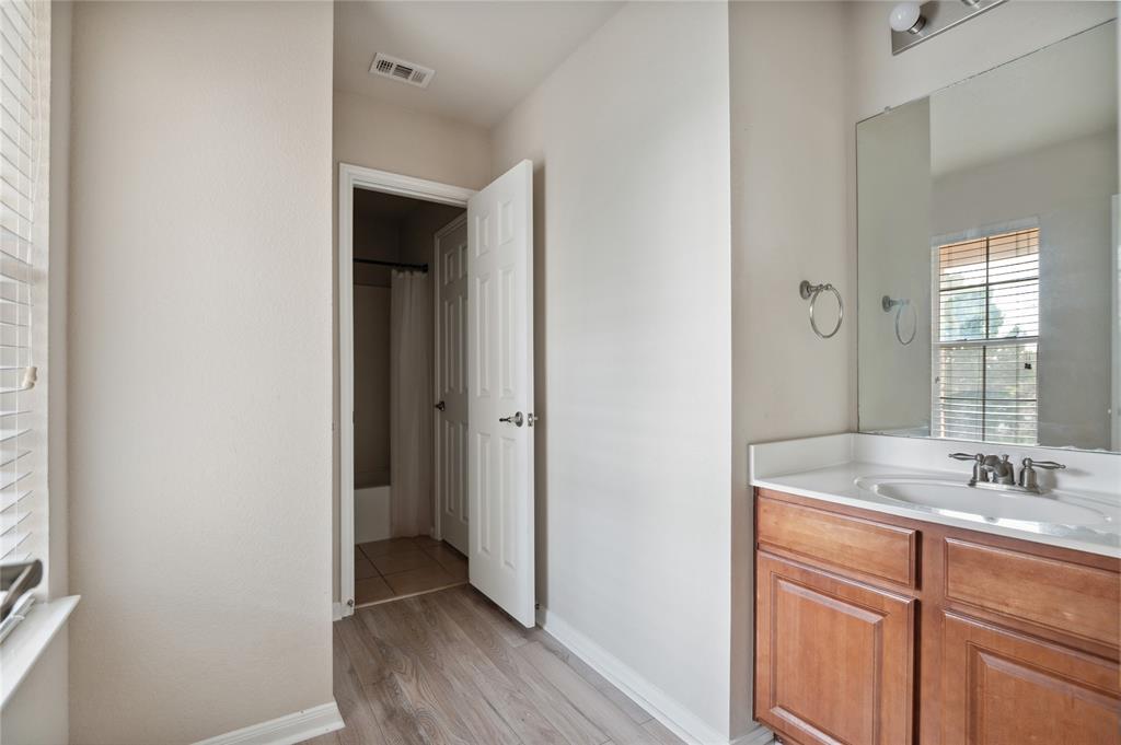 Bathroom with a wood vanity and large mirror beside an open doorway to a tiled area.