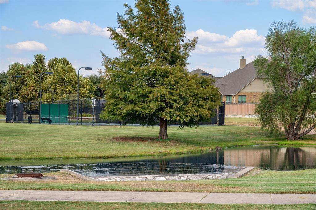 Community pond and lawn beside a fenced sports court and nearby homes.