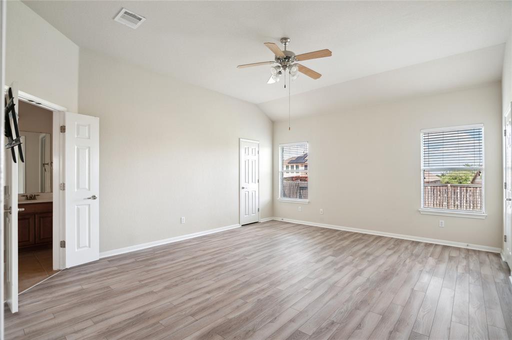 Empty bedroom with wood-look flooring, ceiling fan, and windows with blinds.