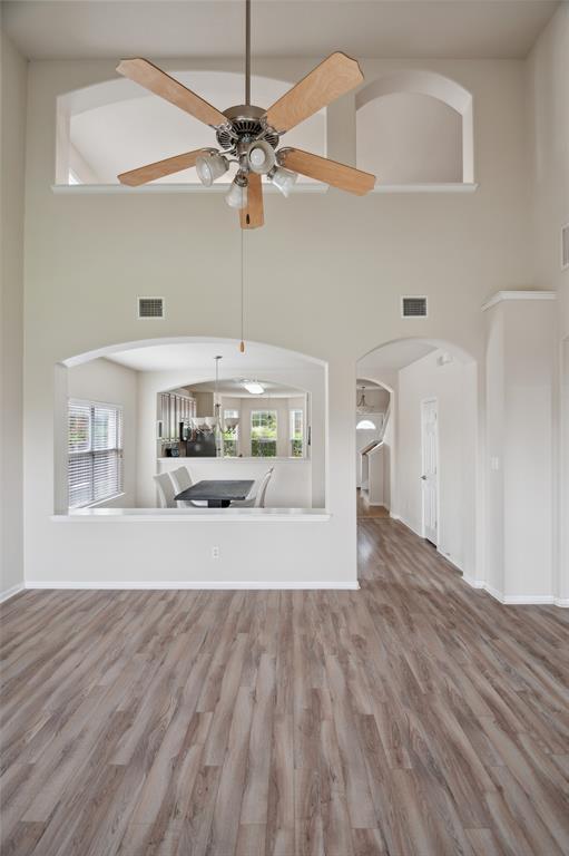 Open living area with high ceilings, wood-look floors, and arched openings to the dining area and hallway.