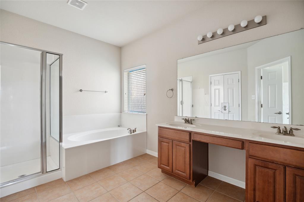 Bathroom with a glass shower, built-in tub beneath a window, and long wood double vanity.