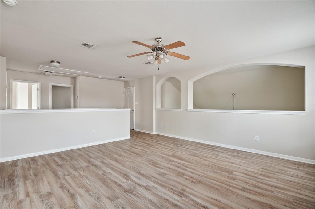 Empty living area with wood-look flooring, a ceiling fan, and arched openings.