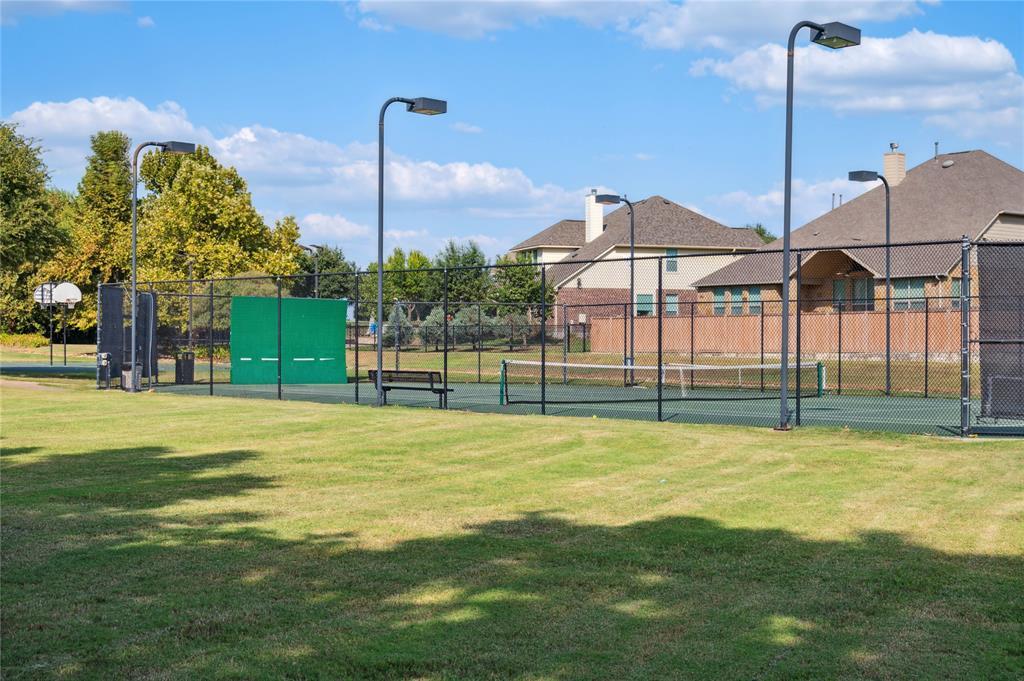 Fenced outdoor court with a basketball hoop, netting, and grassy lawn.