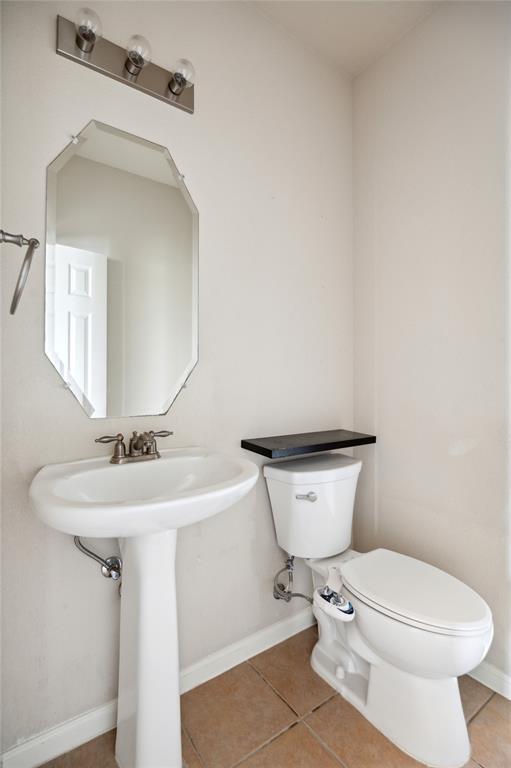 Bathroom with a pedestal sink, faceted mirror, and toilet beneath a dark shelf.