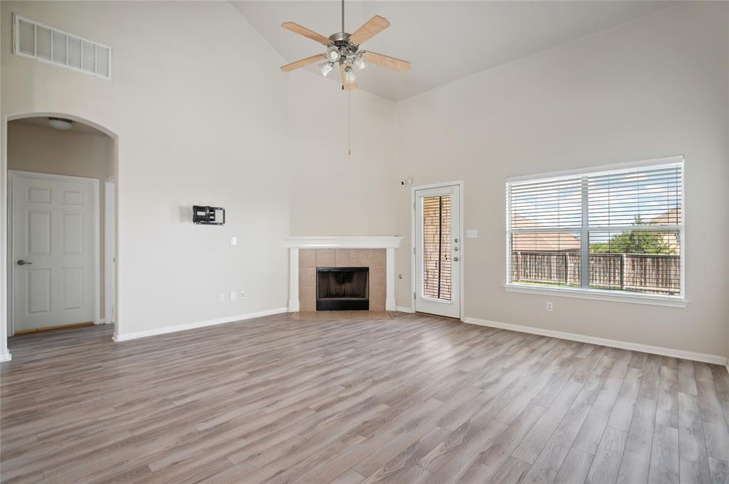 Vacant living room with gray wood-look flooring, a fireplace, vaulted ceiling, and large window.
