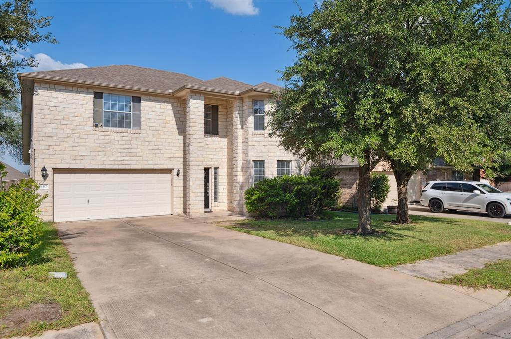 Two-story stone house with an attached garage, wide driveway, and mature trees.