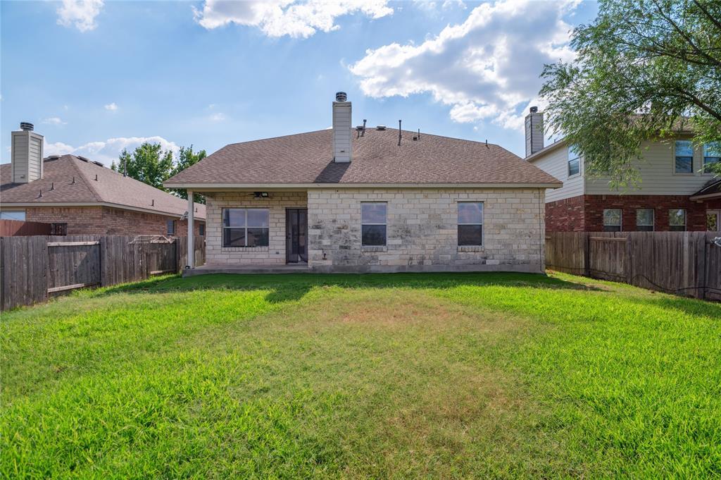Rear of a stone home with a wide grassy backyard enclosed by wood fencing.