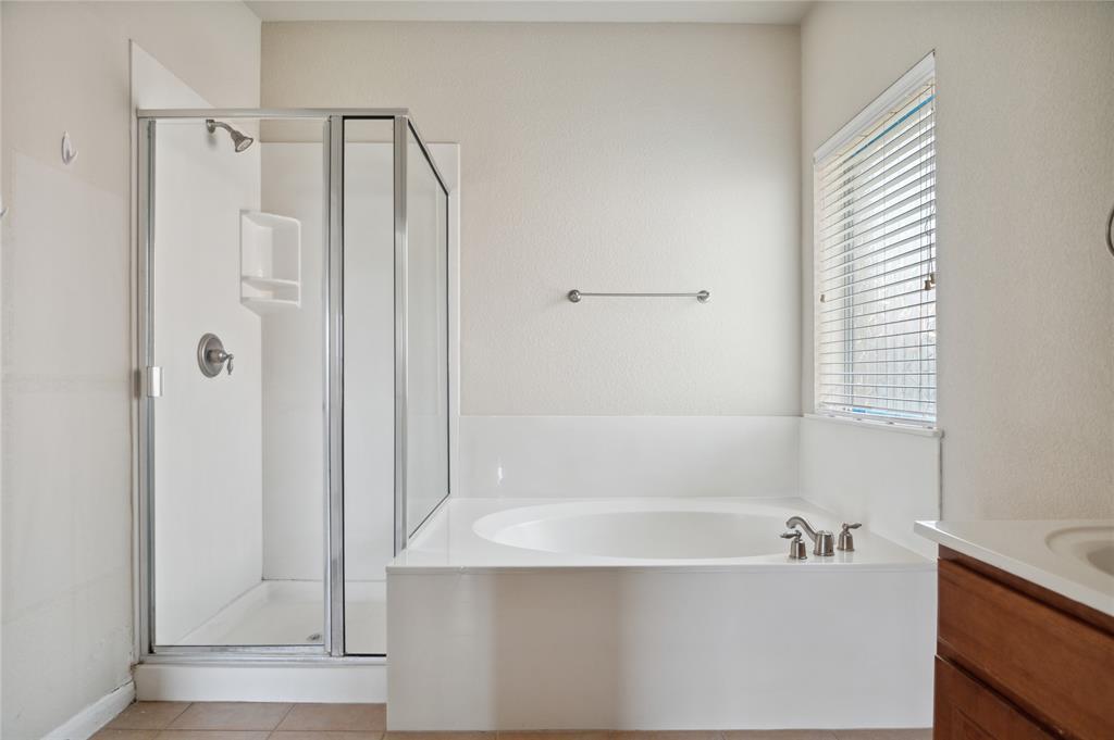 Bathroom with a soaking tub beside a glass-enclosed shower and a window with blinds.