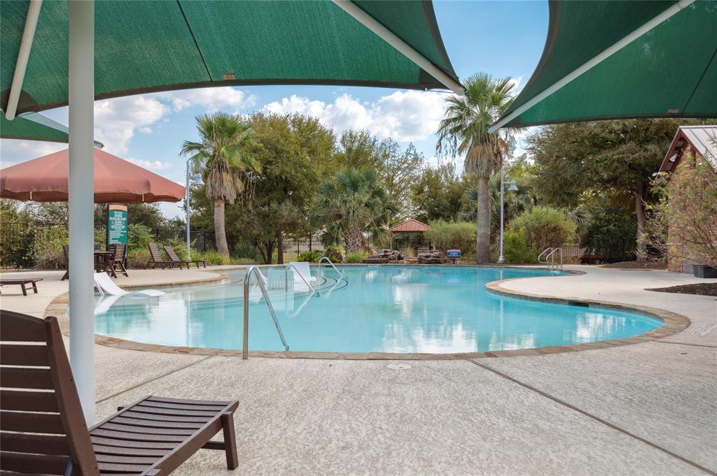 Community pool with curved shallow end, green shade sails, and palm trees.
