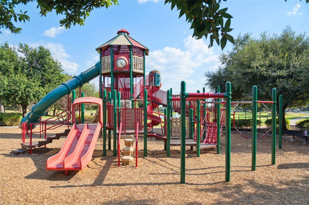 Community playground with colorful slides, climbing structures, and swings beneath leafy trees.