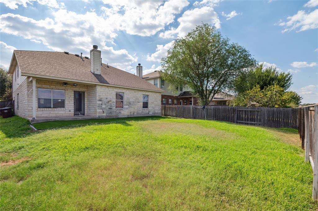 Stone-sided home's rear exterior and fenced grassy backyard beneath mature trees.