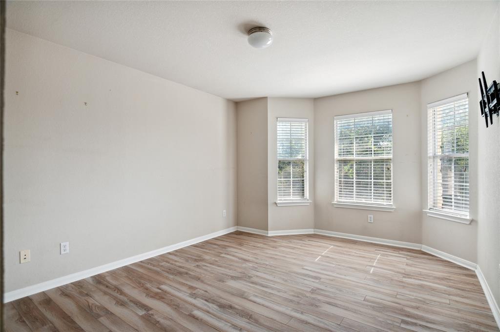 Vacant room with wood-look flooring, three windows with blinds, and a television wall mount.