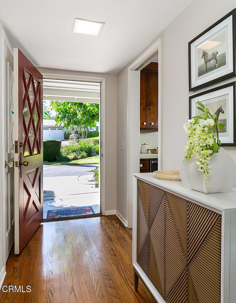 Entryway with hardwood floors, a red diamond-panel door, and a console topped with flowers.