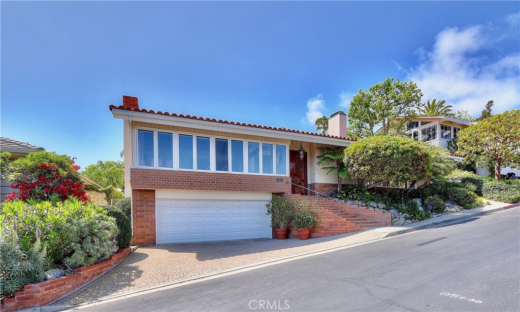 Home exterior with a brick facade, wide garage, and landscaped entrance on a sloping street.