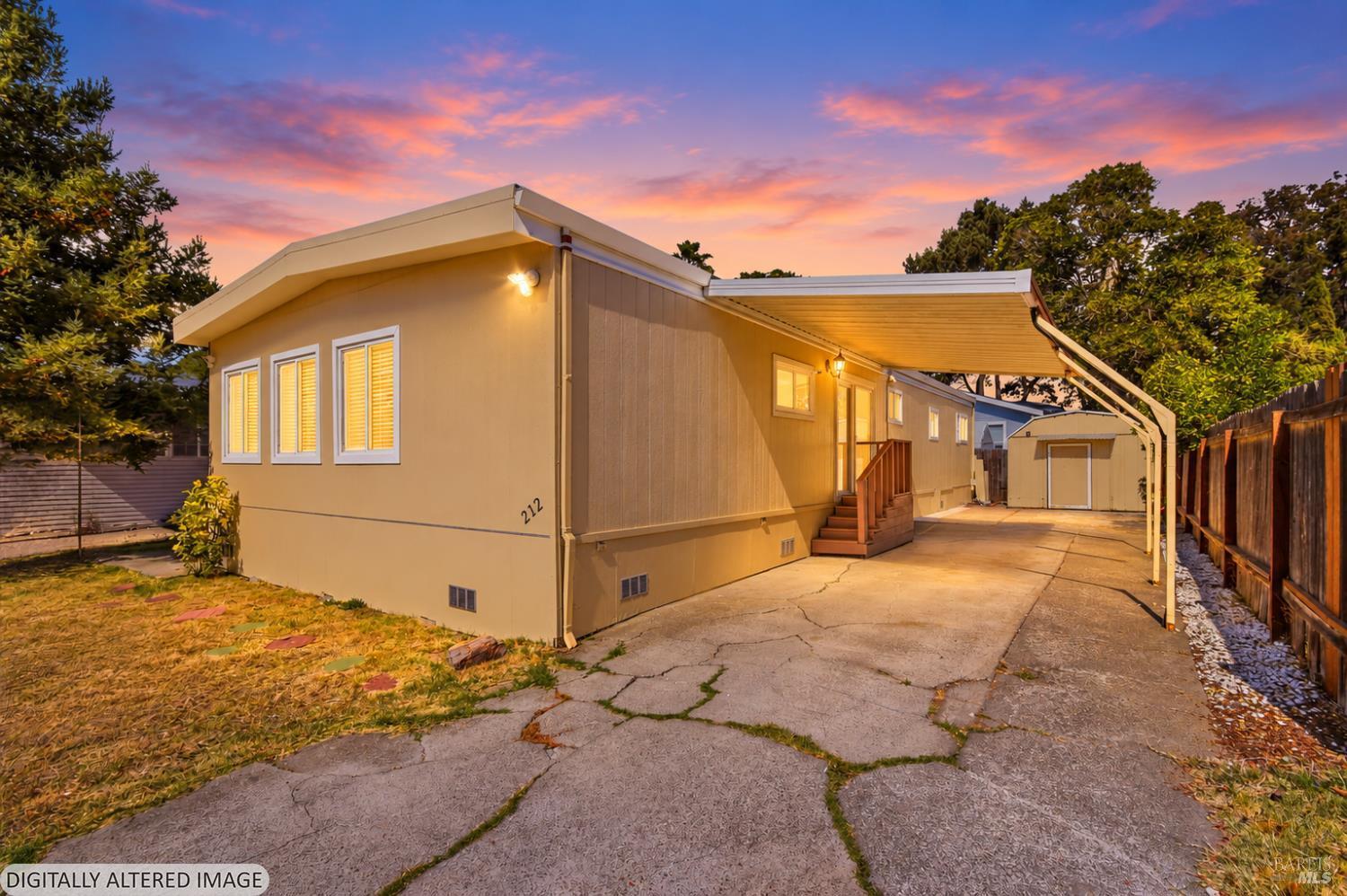 Tan single-story home with a covered carport and detached shed beneath a colorful sunset sky.