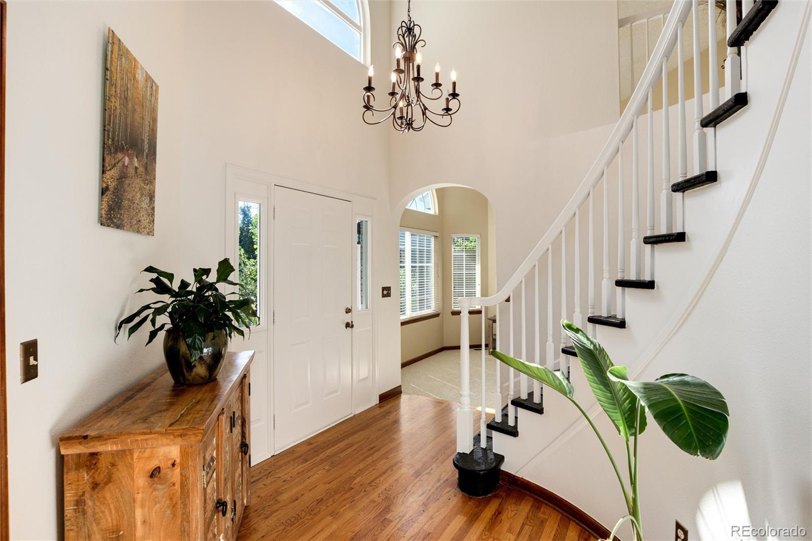 Bright entryway with hardwood floors, a white staircase, and a wooden console table beside the front door.