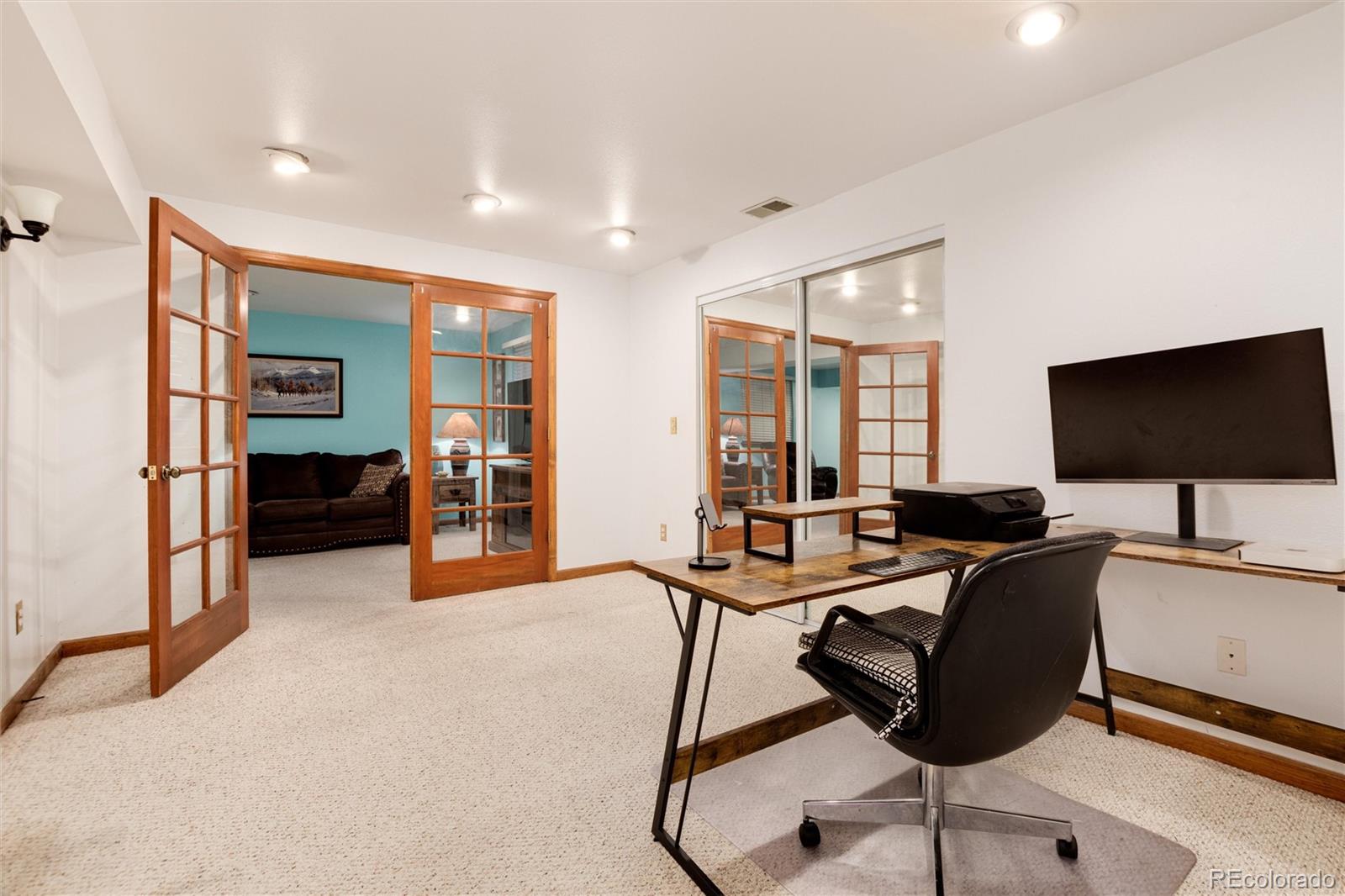 Home office with a desk and swivel chair, opening through wood-framed French doors to a turquoise-walled room.