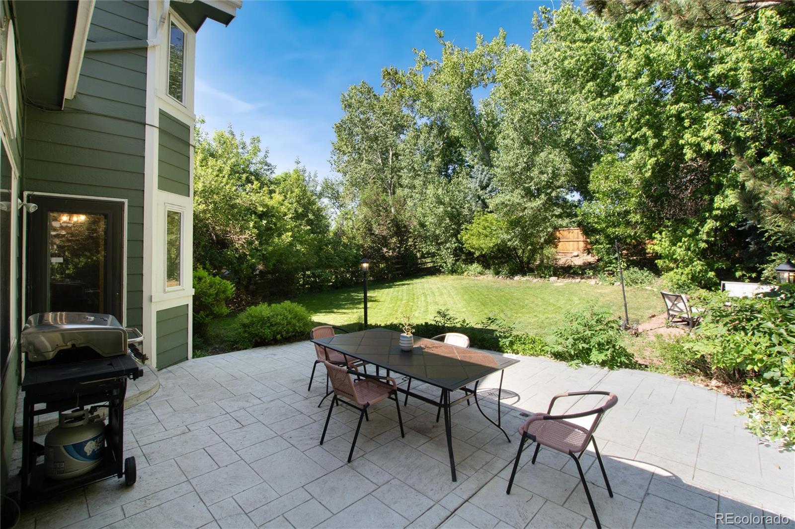 Paved patio with outdoor dining set and grill overlooking a leafy lawn.