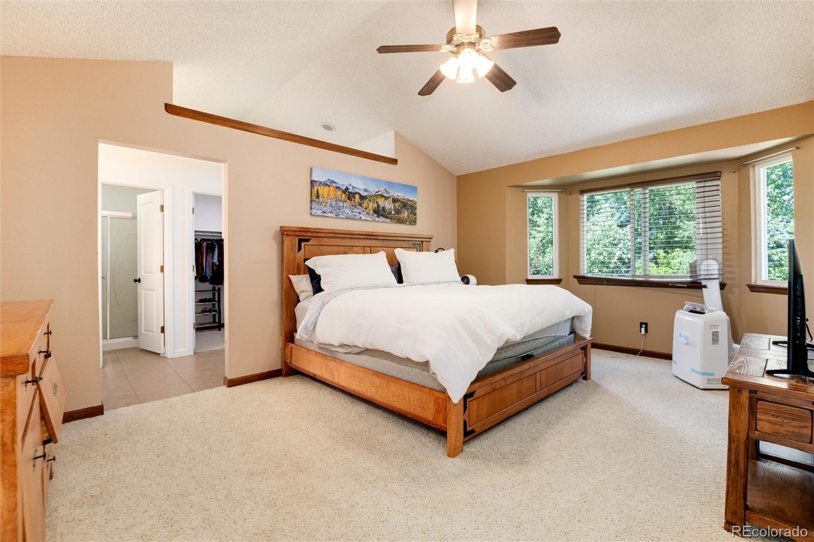 Bedroom with a wooden bed, white bedding, ceiling fan, and windows overlooking greenery.